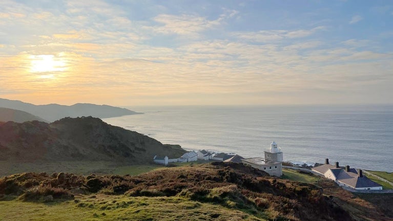 Sunset over the sea with a light house on a cliff in the foreground